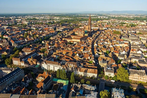 Photographie professionnelle d'une maison strasbourgeoise typique avec architecture alsacienne caractéristique (colombages bois apparents, toiture en tuiles, façade historique rénovée), photographiée de trois-quarts depuis la rue, montrant clairement l'intégration dans le contexte urbain ou semi-urbain de Strasbourg. L'image doit mettre en évidence un projet de rénovation ou restauration bois de qualité, prise en plein jour avec un éclairage naturel optimal. Pas de personnes, pas de texte ou logo visible. La perspective doit être différente des vues précédentes (par exemple, montrer l'environnement urbain immédiat, les connexions avec le tissu bâti voisin, ou des détails architecturaux distincts).